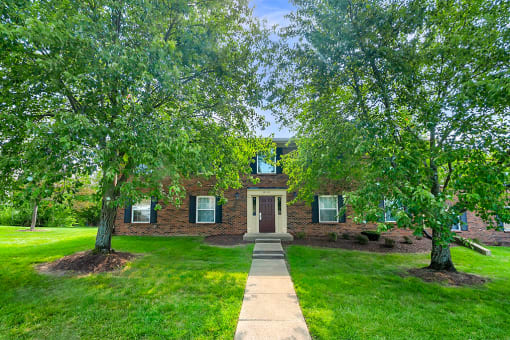Exterior view of Carriage House Apartments in New Albany, featuring a brick building, surrounded by well-maintained grounds and trees in front.