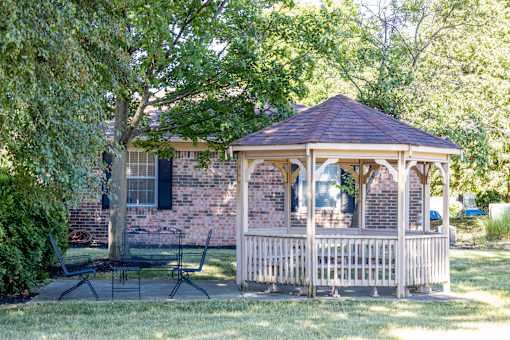 A gazebo is situated in a grassy area in front of a brick house.
