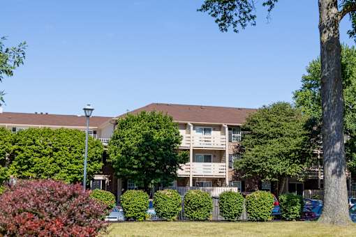 A large building with a brown roof and a balcony is surrounded by green trees and bushes.
