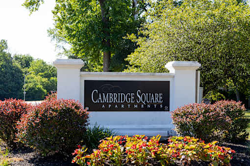 A sign for Cambridge Square Apartments is surrounded by flowers and greenery.