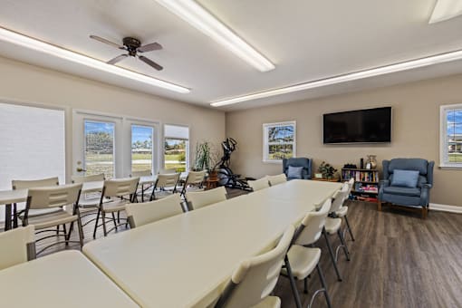 Interior view of the community clubhouse at Fairington Apartments in Lafayette, showcasing a spacious room with chairs, a table and ample natural light.