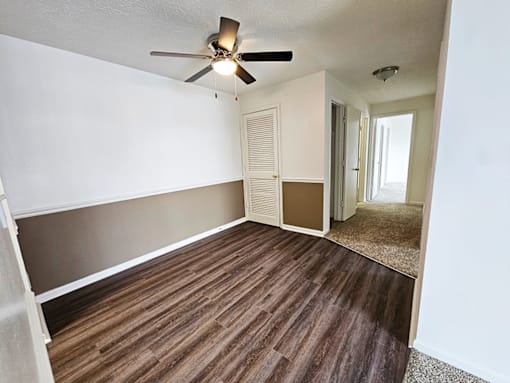 A room with a ceiling fan and brown flooring.