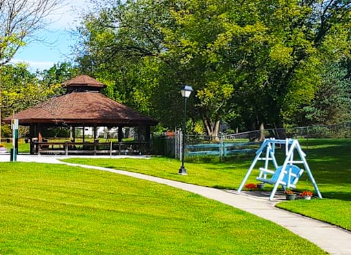 A gazebo sits in a park with a playground in the foreground.