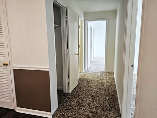 A hallway with a brown carpet and white walls.