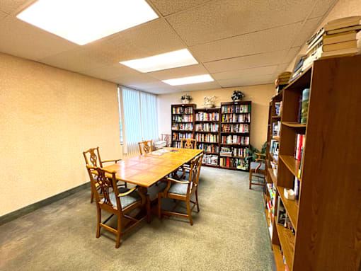 Library room featuring a table, chairs, and bookshelves filled with books at Kentwood Square Apartments.