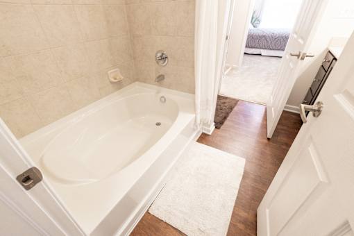 A white bathroom with a tub and a rug on the floor.
