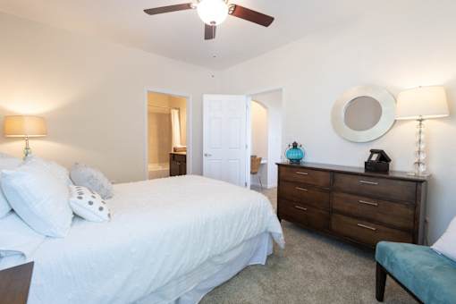 A bedroom with a bed, dresser, and ceiling fan.