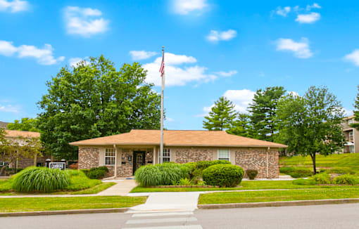 A building with a flag on top is surrounded by greenery and a clear sky.