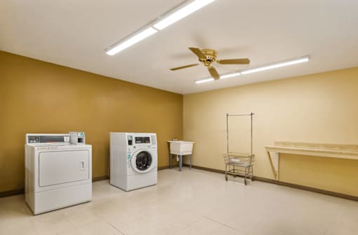 A room with a washer and dryer, a fan, and a shopping cart.