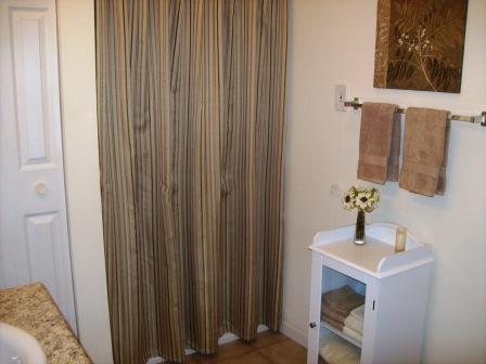 A white cabinet with a vase of flowers on top sits in a bathroom with a brown striped shower curtain.