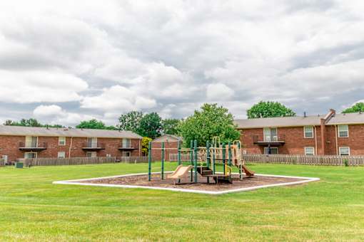 A playground with a slide and swings in the middle of a grassy area.