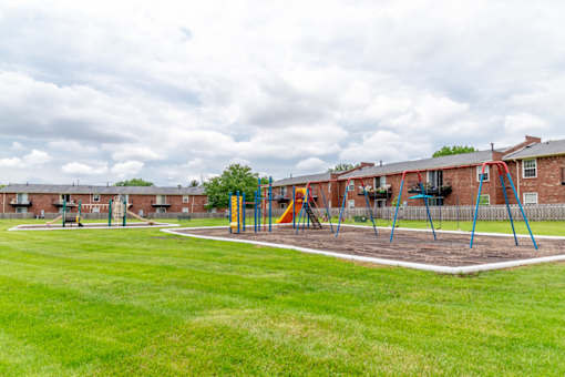 A playground with swings and a slide in front of a brick building.