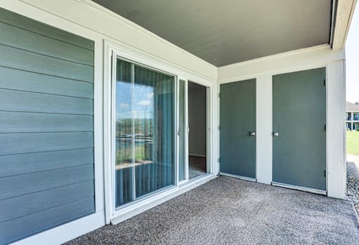 Patio with a sliding glass door at Somerset Lakes Apartments, offering a private outdoor space for relaxation. and a grey door.