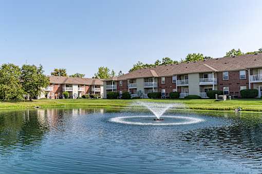 A fountain in the middle of a pond in front of apartment buildings.