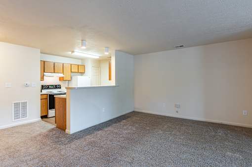A room with a carpeted floor and a small kitchenette.