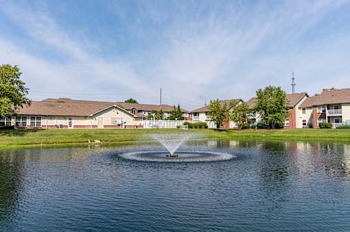 A fountain in the middle of a pond in front of apartment buildings.