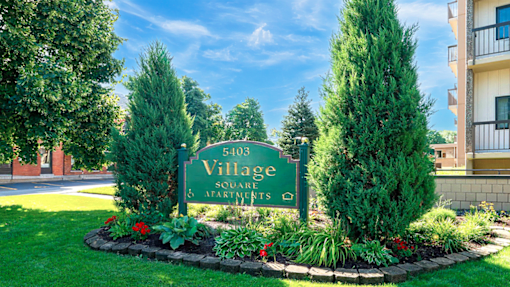 A sign for Village Square Apartments surrounded by greenery.