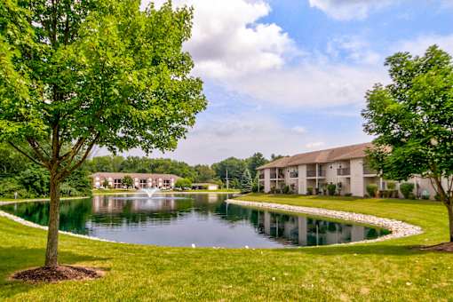 A tree stands next to a pond in front of a building.