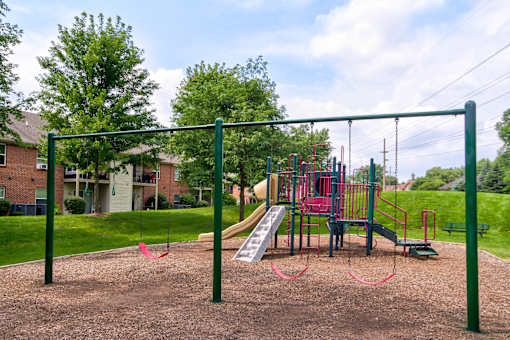 A playground with a red swing set and a green metal frame.