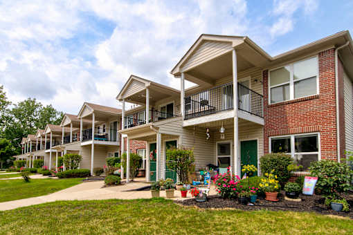 A row of townhouses with green lawns and flower pots in front.
