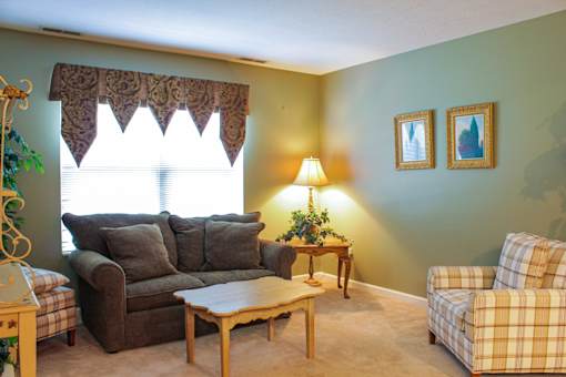 A living room with a brown couch, a plaid chair, and a table with a lamp on it.