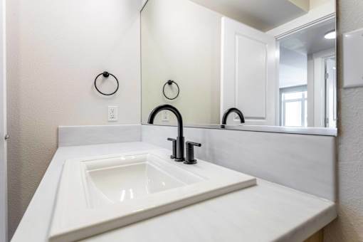 Corner bathroom sink with black faucet and towel ring at The Lyric Apartments, Washington, 98102