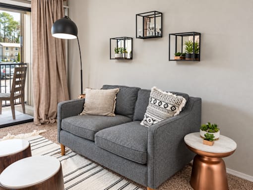 A grey couch with a striped pillow is in the middle of a room with a lamp and a table.