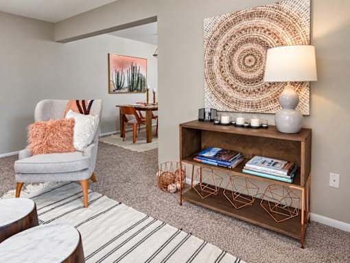 A living room with a grey armchair, a wooden coffee table, a wooden bookshelf, and a large woven wall hanging.