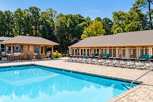 A large swimming pool with a wooden pavilion and lounge chairs.