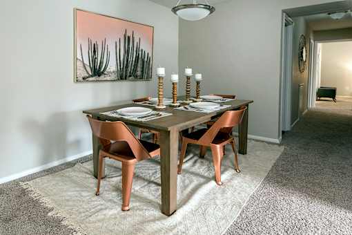 A dining room with a table set for two and a painting of a desert scene on the wall.