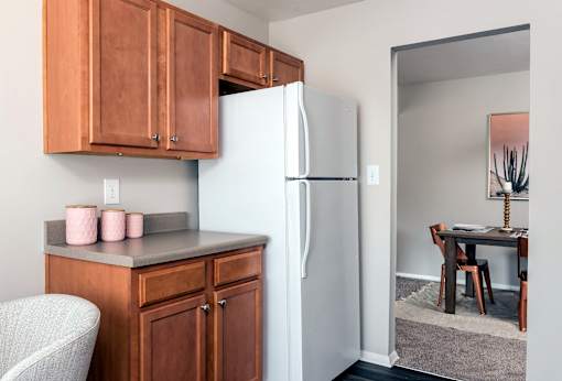 A kitchen with a refrigerator, wooden cabinets, and a chair.