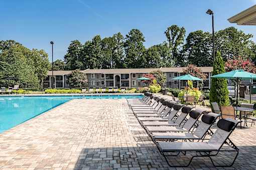 A pool surrounded by chairs and umbrellas with a building in the background.