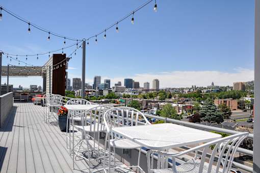 A rooftop patio with white chairs and tables overlooking a city skyline.