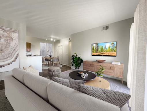 A living room with a grey couch and a painting of a forest on the wall.
