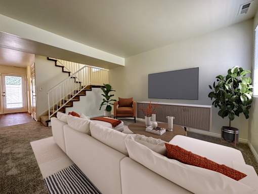 The Ridge at Jordan Landing Apartments, West Jordan, Utah, living room with a white couch and a television, stairs to second floor in the backround and entrance to kitchen.