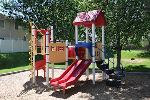 A playground with a red slide and a red and white swing set.