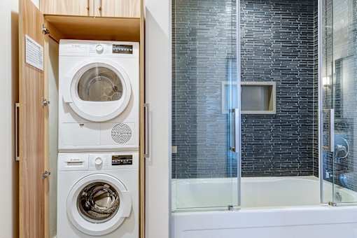 Beautiful bathroom in Maxfield loft with beautiful blue tile in the shower/tub, stacked washer and dryer concealed by beautiful wood cabinetry, and a modern vanity.