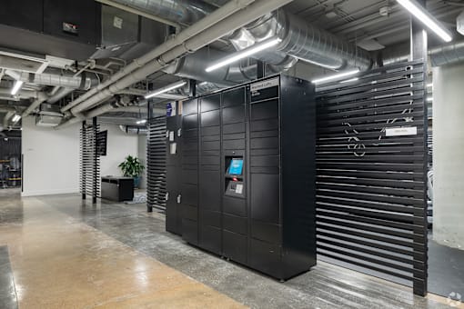 A large black server unit in a room with a concrete floor and a wall of vertical pipes.