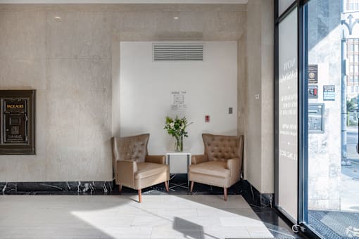 Two tan chairs are placed in front of a wall with a framed picture.