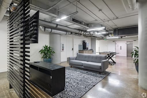 A modern office space with a black cabinet, grey sofa, and a patterned rug.