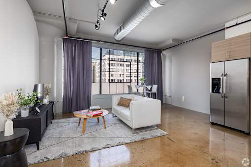 A living room with a white couch, a coffee table, and a large window with curtains.