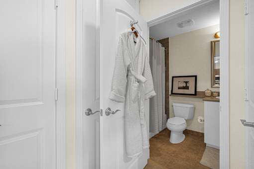 A white bathroom with a toilet, sink, and a white robe hanging on the door.