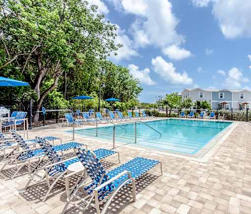 A pool surrounded by blue chairs and trees.