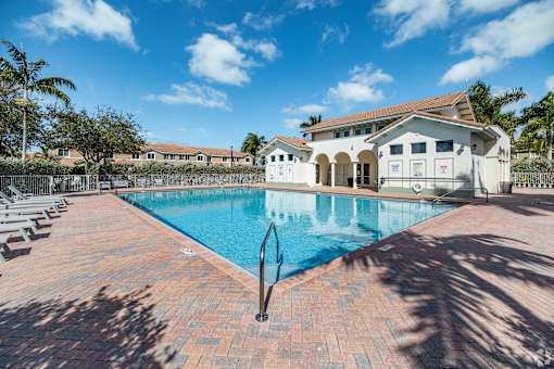 A large swimming pool surrounded by a brick patio and a white building in the background.