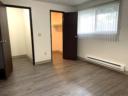 A room with a wooden floor and a window with blinds.