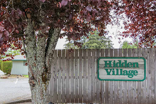 A sign that says Hidden Village is on a wooden fence.