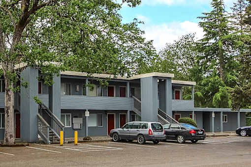 A grey building with a red door and a tree in front.