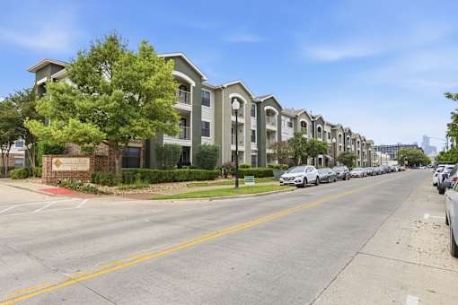 A row of apartment buildings with cars parked on the street.