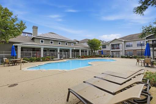 A pool area with sun loungers and a building in the background.
