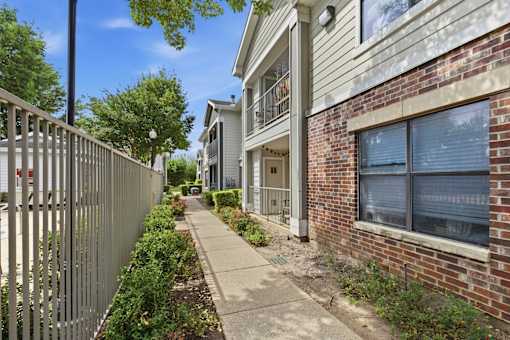 A sidewalk runs between a metal fence and a brick building.